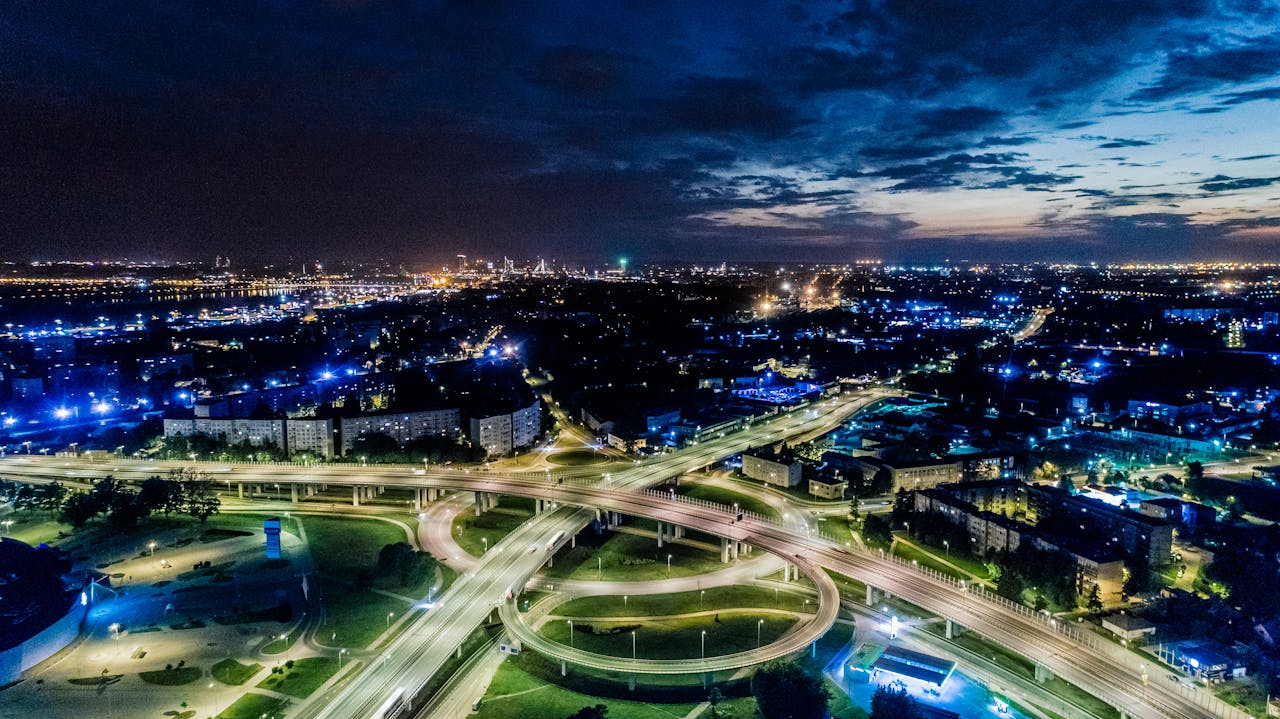 Vibrant cityscape aerial view of illuminated highways and urban skyline at twilight.